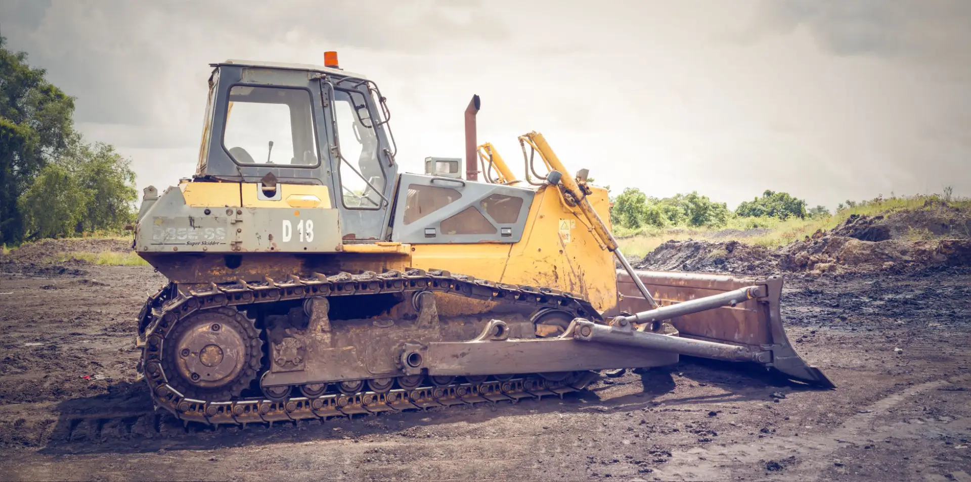 A bulldozer working muddy ground on a construction site under a cloudy sky